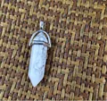 Detail of a hexagonal white marble stone pendant with silver metallic bail on a woven mat - Howlite