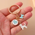 Portachiavi barboncino cartone animato con osso blu e ciondoli a cuore tenuto in mano - Cane