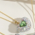 Macro di un ciondolo a cuore dorato con gemma verde e strass arcobaleno incastonati - Zirconia Verde (XL2601-1)