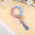 Detail of beaded silicone wristlet with wooden disc, blue tassel and gold clasp - Light Blue Rainbow Stripe