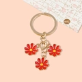 Golden keychain featuring three vibrant red enamel flowers with yellow centers - Red