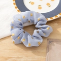 Detailed view of a blue fabric hair scrunchie featuring gold heart foil patterns - Blue
