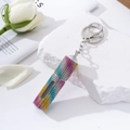 Close-up of rainbow rhinestone perfume bottle keychain on a white decorative stone - Rainbow 1