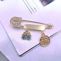 Makroaufnahme der goldenen Sicherheitsnadel-Brosche mit Hamsa-Anhängern und blauen Steinen - Hellblauer Kreis