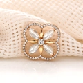 Detailed view of a gold four-leaf clover accessory with sparkling crystals on woven fabric - White