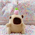 Plush Capybara keychain with pink peach hat and golden lobster clasp on colorful background - Light Brown Peach + Gold Clip