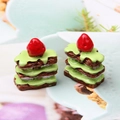 Makroaufnahme von Miniatur-Erdbeerkuchen aus Harz mit grünem Guss und feinen Details - Dunkelkaffee + Matcha