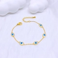 Detailaufnahme eines goldenen Armbands mit blau-weißen Evil-Eye-Anhängern auf weißem Dekor - Ovales Auge