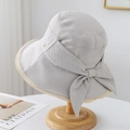 Detalle del sombrero de sol beige claro con textura plisada y un lazo decorativo lateral - Gris