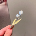 Silver tulip hair clip with white petals and yellow enamel leaf detail held by hand - Blue