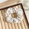 White floral lace scrunchie with blue and red patterns on a beige jewelry tray - Label Blue Bow