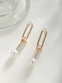 Detalle macro de pendientes ovalados chapados en oro con perlas blancas y líneas geométricas - Pendientes largos de tres perlas