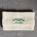 Close-up of off-white knitted headband featuring green Stockholm Sweden embroidery detail - White