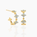 Close-up of gold C-shaped earrings with blue zircon flowers on a reflective white base - Golden with Blue Stone