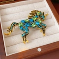 Broche licorne vintage dorée avec strass bleus et verts dans une boîte à bijoux - Broche Bleue