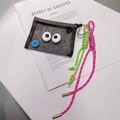 Détail d'un porte-clés pochette en filet avec yeux et cordons tressés sur un magazine - Sac Noir A12