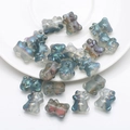 Close-up of translucent blue-green teddy bear crystal beads scattered on a white plate - Frosted Rose Red Green