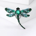 Silver insect dragonfly brooch with green and blue gemstones on a white pedestal - Green