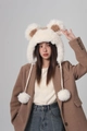 Detail view of plush bear ears and braided ties with large pom-poms on a cream bucket hat - Beige