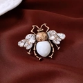 Dettaglio macro di spilla a ape vintage dorata con strass e perla su velluto scuro - Spilla 33# - Bronzo - Bianco - Trasparente