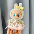 Labubu doll in green hoodie and beige rabbit dress with a yellow bow accessory - Safety Pin Bunny Head Skirt / First And Second Generation Keychains Are Compatible With La Cloth Dolls. Dolls Not Included.