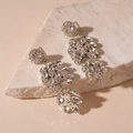 Détail de boucles d'oreilles feuilles argentées avec strass brillants sur socle en pierre - Argenté