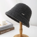 Close-up of dark grey curly faux fur bucket hat with silver logo on wooden stand - Gray