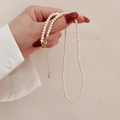 Elegant natural pearl necklace with gold clasp held by a hand against a beige background - Pearl Necklace (Color Retention)