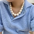 Close-up of elegant gradient pearl necklace worn with a textured blue polo shirt - Large Bead White Pearl Necklace