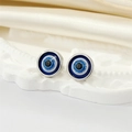 Close-up of resin Evil Eye stud earrings on a white embossed tray and silk fabric - Silver Blue Glitter Eye