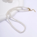 Collana di perle in acciaio al titanio con perle bianche e fibbia dorata su sfondo bianco - Stile Perla Rotonda da 5mm