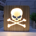 Close-up of square 3D wooden night light with glowing skull and crossbones cutout - Skull/15cm