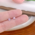 Macro close-up showing small pink round zircon stud earrings held on a fingertip - Vertical Prong No.4 / Pink