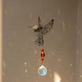 Détail d'un attrape-soleil colibri en métal projetant des reflets arc-en-ciel sur le mur - Colibri