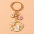 Dettaglio di un portachiavi dorato con sagoma di gatto bianco e ciondoli a fiori di ciliegio - Ghirlanda di Gatto / Oro