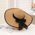 Straw sun hat with large brim and black bow decoration on a wooden display stand - Khaki & Black