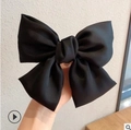 Elegant oversized black fabric bow hair clip held by hand for a minimalist aesthetic - Black Satin Large Bow