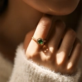 Close-up of adjustable gold ring with green emerald halo stone on model wearing a sweater - Adjustable Open / Green (KR0042-2)