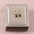 Detalle de pendientes de aro dorados con colgantes rectangulares de gema azul en caja - 26b06021-black diamond earrings