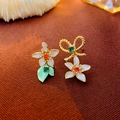 Nahaufnahme asymmetrischer Schleifen-Ohrringe mit weißen Blüten und bunten Zirkon - Goldene asymmetrische Blumenohrringe (Silbernadel)