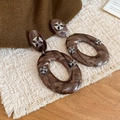 Detalle de pendientes ovalados de resina marmolada con cruces decorativas de plata - Marrón