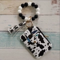 Detail view of silicone bead bracelet with cow print wallet and tassel on wooden surface - Black and White Cow