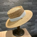 Detail eines klassischen Strohhuts mit weißem Band auf einem Holzständer vor grauer Wand - M (56-58cm) / Khaki Mit Beigem Band