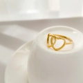 Dettaglio di anelli a cuore dorati intrecciati su una base minimalista in ceramica bianca - US 6 / Doppio cuore traforato
