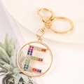 Macro shot of gold alphabet E keychain with colorful rhinestones on a white plate - Letter E