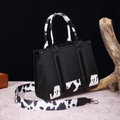 Detail of black faux leather tote with cow print trim and braided side accents - Small Black (Cow Print)