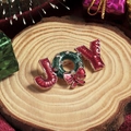 Broche de Noël JOY avec couronne verte et nœud rouge sur fond de bois naturel - Lettre JOY avec Noeud