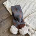 Detailed knit texture of children's grey scarf featuring cute cream white faux fur pom-poms - Gray