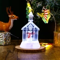 Macro shot of glowing Christmas church ornament with snowman figurine on wooden base - Snowman