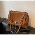 Detail of a brown leather shoulder bag with a silver metal lock on a black sofa - Brown